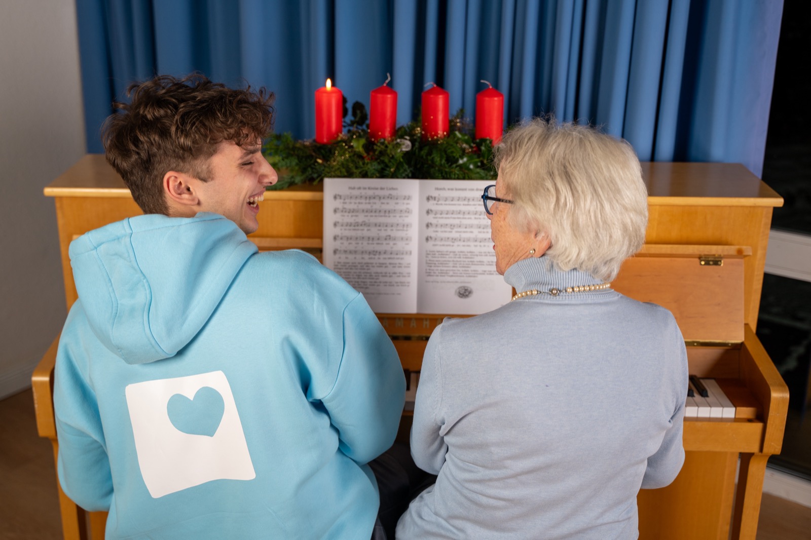 Junges Paar und Seniorin am Klavier mit Adventskerzen